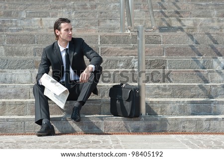 Young business man with newspaper sitting on the stairs.