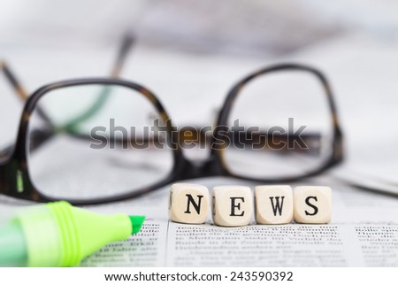 News formed by wooden letters, on top of newspapers with glasses and pen