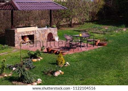 Backyard Patio Area with Fireplace and Furniture. Green Party area. Barbecue Area. Stone.