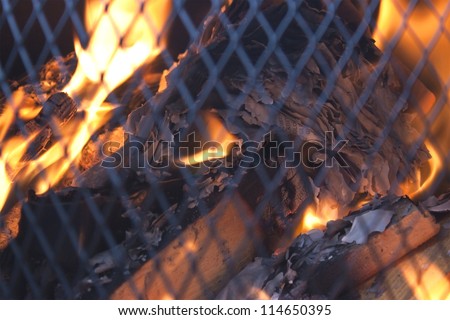 fire safely behind a mesh grill, burning wood and papers