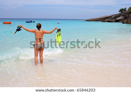 Young woman holding snorkel, mask and fins; standing at the beach of Similan Island, Thailand