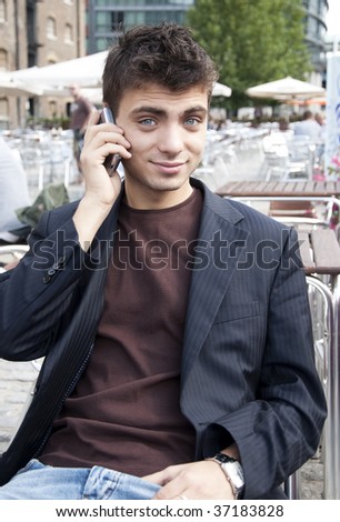 Young handsome guy in outdoor cafe with cell phone has surprised face