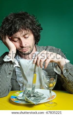 Man bored sticking table knife into a heap of dollars. With money on the dish inside of food.
