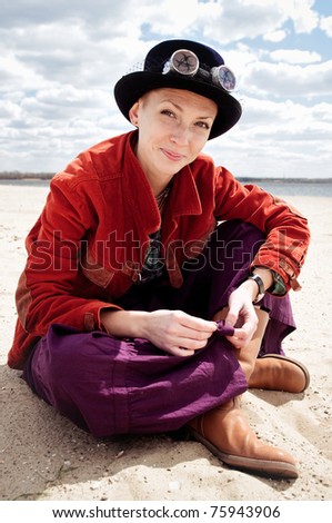 woman wearing boots and weird glasses sitting on a beach