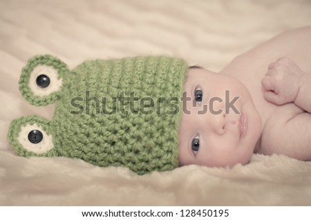 Newborn baby wearing a frog crochet hat and looking at the camera