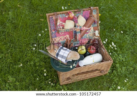 picnic basket on lawn with fresh olive-baguette, milk, apple and sausages, bread and pieplant juice.