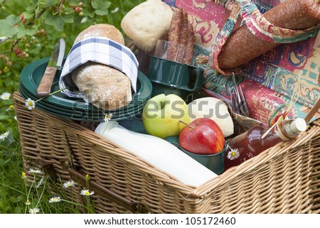 outdoor dining : picnic basket on lawn with fresh olive-baguette, milk, apple and sausages, bread and pieplant juice.