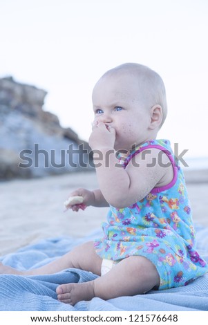 cute baby girl eating a snack (bread) on the beach.