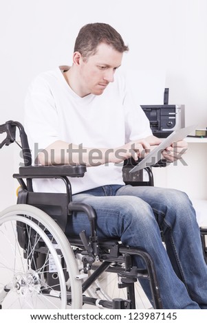 man on wheelchair working in a home office, using a tablet computer