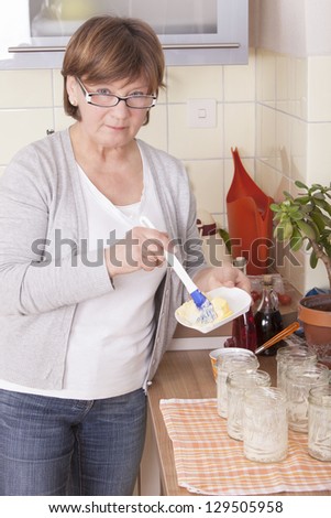 senior woman baking homemade chocolate cake, using butter for glass jars. baking chocolate/stracciatella cake in a glass jar.
