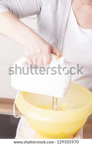 senior woman baking homemade chocolate cake, using a mixer. baking chocolate/stracciatella cake in a glass jar.
