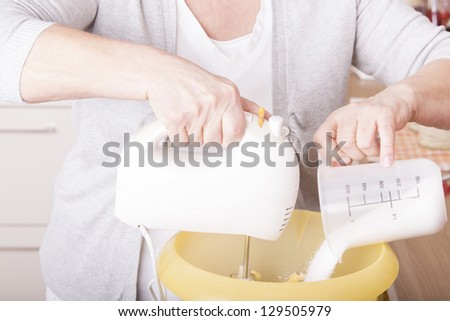 senior woman baking homemade chocolate cake,using a mixer and milk. baking chocolate/stracciatella cake in a glass jar.