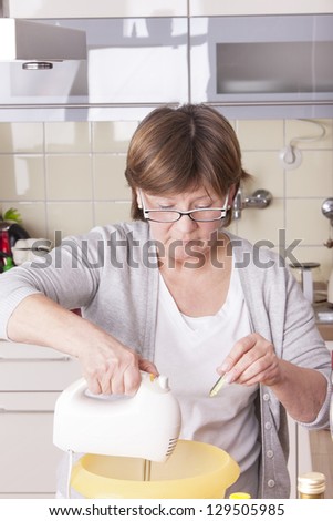 senior woman baking homemade chocolate cake, using a mixer and a bottle with flavor. baking chocolate/stracciatella cake in a glass jar.