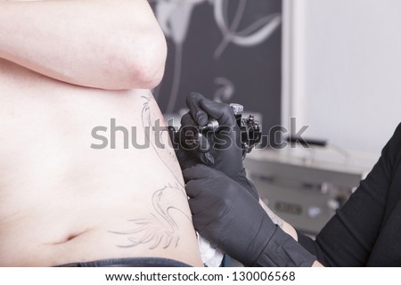 female tattoo artist at work. ( property release supplied includes tattooists\' tattoo and artwork )