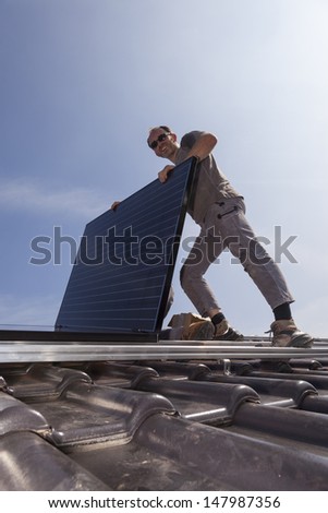 worker installing alternative energy photovoltaic solar panels on the roof of a single family house