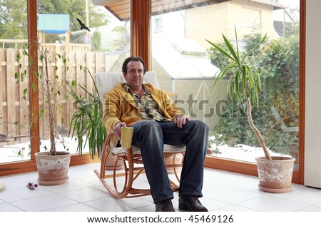man sitting in a rocking chair inside conservatory and having a cup of coffee