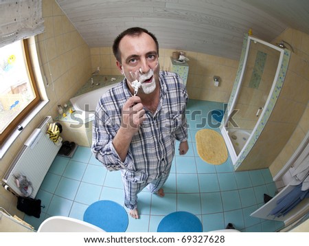 after a sleepless night with a hangover, a very tired man with a bad mood standing in the bathroom shaving. Image taken with a fish-eye lens.