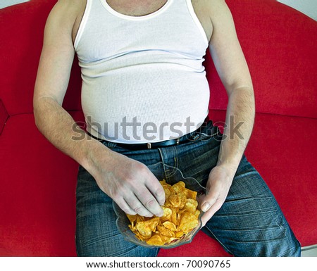 fat man on red couch eating potato chips.