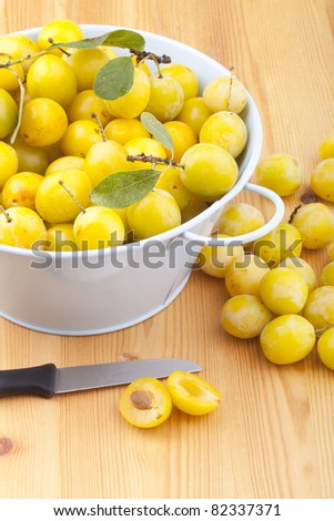 studio-shot of small yellow plums also known as mellow mirabelles, on a wooden countertop. one is halved with a knife.