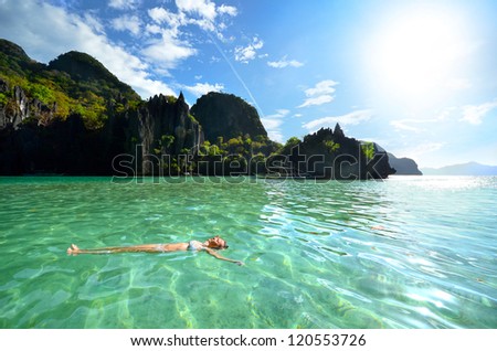 Woman resting on his back in the crystal clear water of island rock in the sun. El Nido