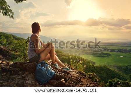 A Girl Sits On The Edge Of The Cliff And Looking At The Sun Valley And Mountains