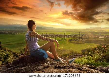 A woman sits on the edge of the cliff and looking at the sun valley and mountains