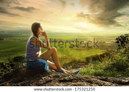 Woman sits on edge of cliff and looking at sun valley and mountains