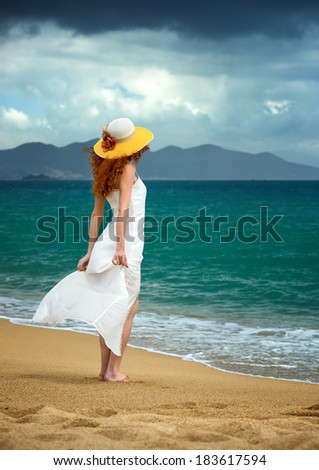 Lonely woman in a white dress standing at the sea shore and watching the storm