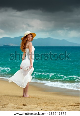 Lonely woman in a white dress standing smile  at the sea shore and watching the storm