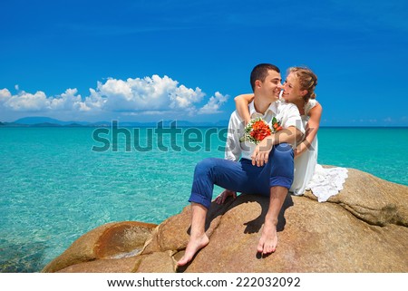 happy romantic wedding couple in love, groom and bride in white wedding dress sitting on the beach