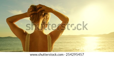 A back side view on a wonderful young woman watching to sea and raising her hands on sunrise