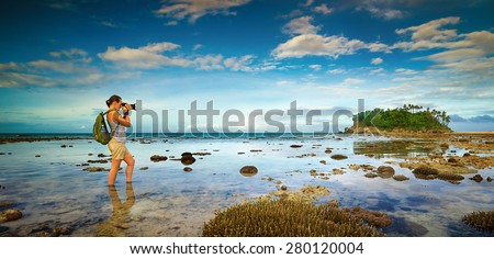 standing in the water traveler woman with backpack taking a landscape of nearby amazing island. Traveling along Asia, active lifestyle concept