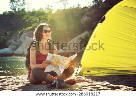 Early in the morning young woman tourist sit near the tent reading the map and thinking about future walking tour