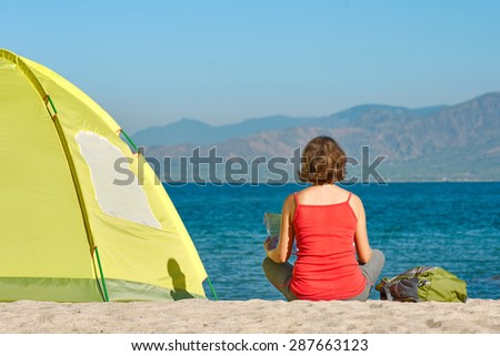Young woman tourist sit near the tent looking the map and thinking about future walking tour