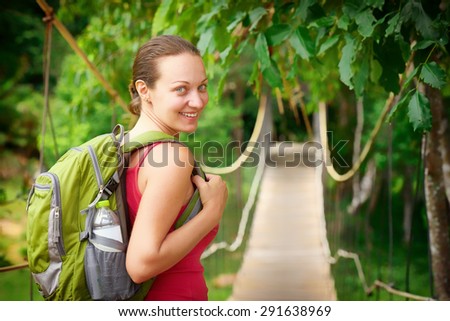 Hiking woman - hiker walking on bridge in rain forest.\
Hiker. Woman hiking smiling happy on trek with backpack during summer outdoors activity.