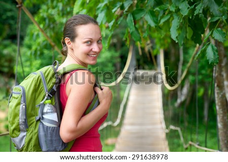 Hiking woman - hiker walking on bridge in rain forest.\
Hiker. Woman hiking smiling happy on trek with backpack during summer outdoors activity.