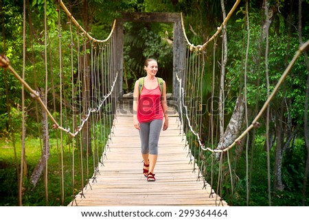 Hiking woman - hiker walking on bridge in forest.  Traveller. Woman hiking smiling happy on bridge with backpack during summer outdoors.