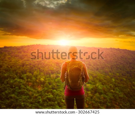 Travelling woman with backpack looking green mountains and inspiring sunset  with dramatic clouds. Tourist girl traveling along Asia, active lifestyle concept