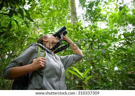 Tourist looking through binoculars considers wild birds in the rain forest.\
Bird watching tours