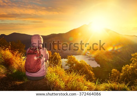 Woman with backpacker enjoying sunrise view at summit top in high mountain volcano Rinjani. Island Lombok, Indonesia. \
Traveling along mountains, freedom and active lifestyle concept