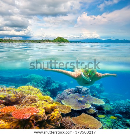 Young woman swimming on the bright coral reef in the sea on a background of a tropical beach. Lombok, Indonesia
