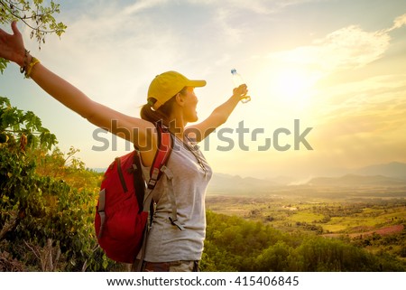Happy traveler with backpack and bottle of water standing on top of mountain and enjoying valley view with raised hands.\
Mountains landscape, travel to Asia, happiness emotion, summer holiday concept