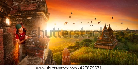 Woman traveler with a backpack explores the ancient temple on a background of beautiful sunrise with balloons. Bagan, Myanmar.\
Traveling along Asia, active lifestyle concept.