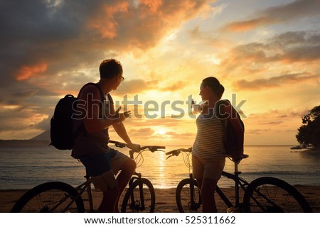 Couple travellers with bicycles watching sunset. Summer nature background with beautiful Sky and Sea. Active leisure concept.