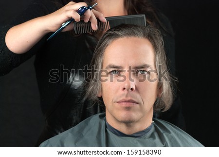 Close-up of a serious man looking to camera while his hair is combed in preparation for having it cut off for a cancer fundraiser.