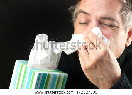 Close-up of a man blowing his nose while holding a tissue box.