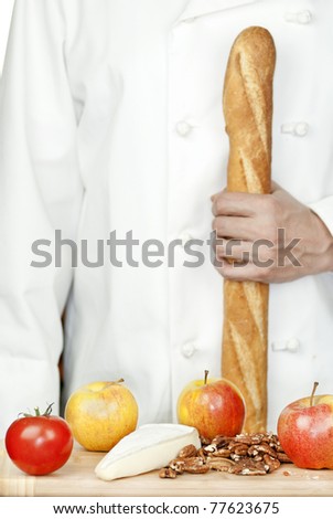 Close-up of a chef holding a baguette in front of a bamboo cutting board of apples, brie and pecans.