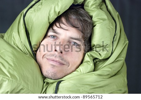 Close-up of a happy man wrapped up in a down mummy sleeping bag.
