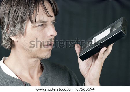 Close-up of a man looking at a video tape in confusion.