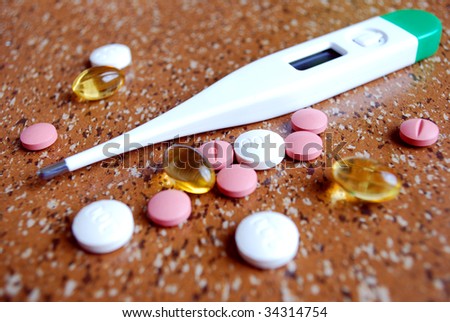 close-up of a clinical thermometer and various clororful capsules and tablets